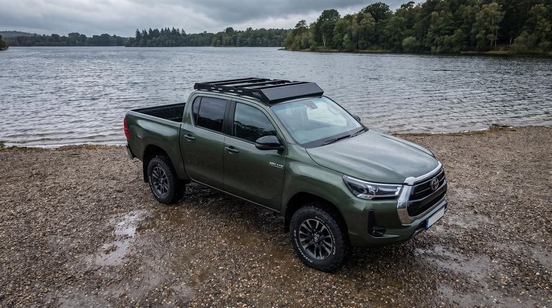Green Toyota Hilux double cab with a low-profile black platform roof rack on a lake shore